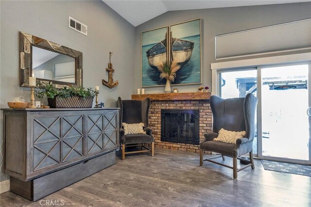 living area featuring visible vents, a fireplace, wood finished floors, and vaulted ceiling