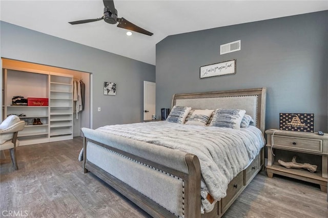 bedroom with a ceiling fan, wood finished floors, visible vents, lofted ceiling, and a spacious closet