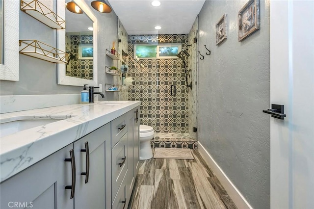 bathroom featuring toilet, wood finished floors, a tile shower, a textured wall, and vanity