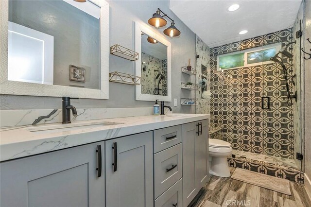 full bath with double vanity, toilet, a tile shower, and a sink