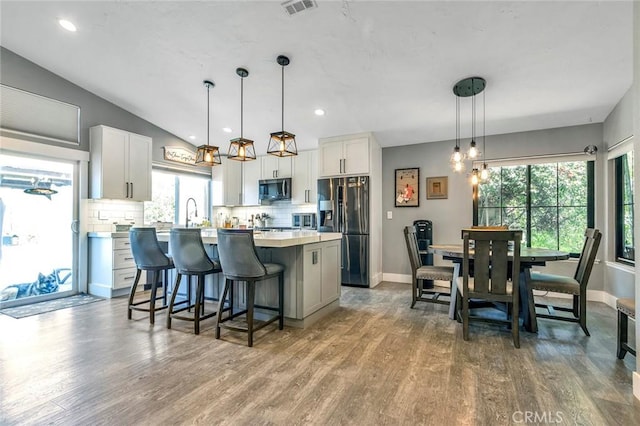 kitchen with refrigerator with ice dispenser, stainless steel microwave, wood finished floors, a center island, and light countertops