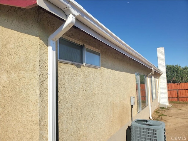 view of side of property with stucco siding, central AC, and fence