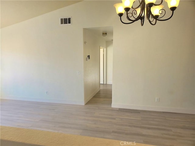 empty room with visible vents, baseboards, vaulted ceiling, light wood-style floors, and a notable chandelier