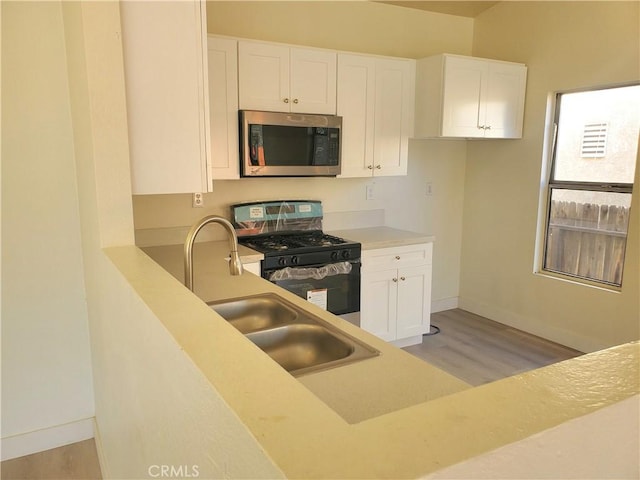 kitchen with light wood-style flooring, light countertops, white cabinets, gas range, and stainless steel microwave