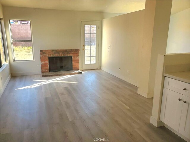 unfurnished living room with a brick fireplace, wood finished floors, and baseboards