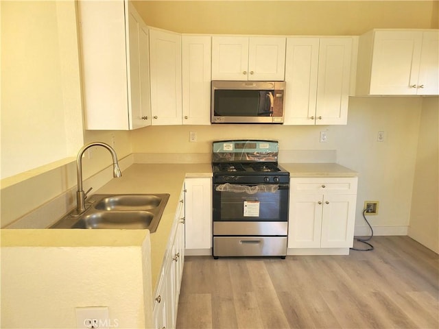 kitchen with a sink, appliances with stainless steel finishes, white cabinets, and light wood finished floors