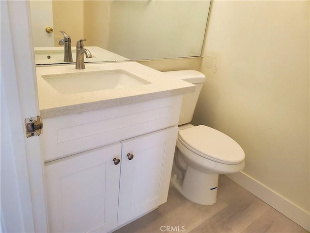 half bath with toilet, vanity, baseboards, and wood finished floors