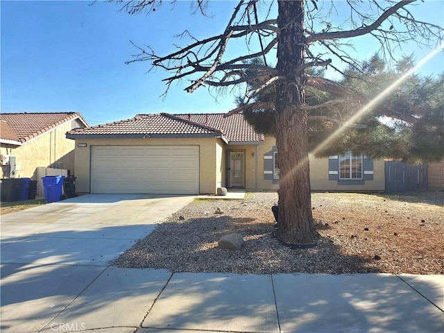 view of front of property with stucco siding, driveway, a tile roof, fence, and an attached garage