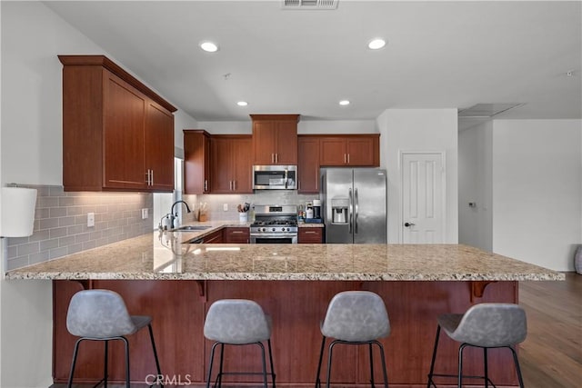 kitchen featuring a peninsula, a sink, stainless steel appliances, a kitchen breakfast bar, and backsplash