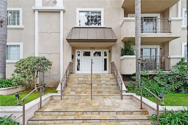 property entrance featuring a balcony, stucco siding, metal roof, and a standing seam roof