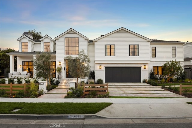 modern farmhouse style home featuring a fenced front yard, driveway, an attached garage, and a porch