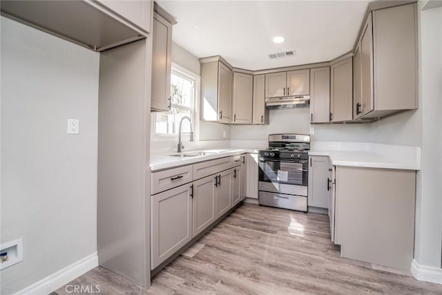 kitchen with stainless steel range with gas cooktop, under cabinet range hood, gray cabinets, light wood-style flooring, and a sink