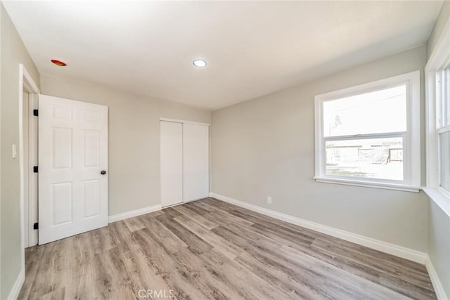 unfurnished bedroom featuring recessed lighting, a closet, baseboards, and light wood finished floors