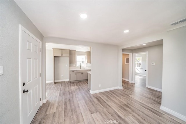 unfurnished living room featuring light wood-style floors, baseboards, a wealth of natural light, and a sink