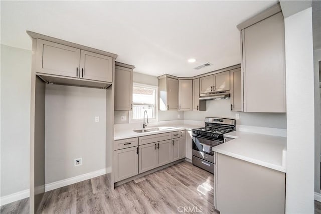 kitchen with a sink, stainless steel range with gas cooktop, under cabinet range hood, and gray cabinetry