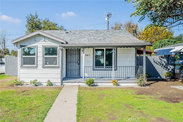 bungalow-style home with covered porch, a shingled roof, a front lawn, and fence