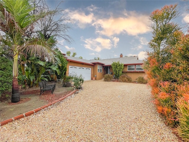 ranch-style house with a garage, gravel driveway, a chimney, and stucco siding