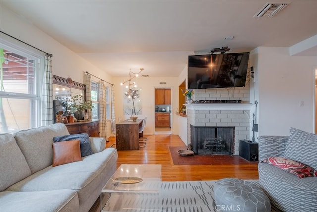 living area featuring visible vents, a brick fireplace, light wood-style flooring, and a chandelier