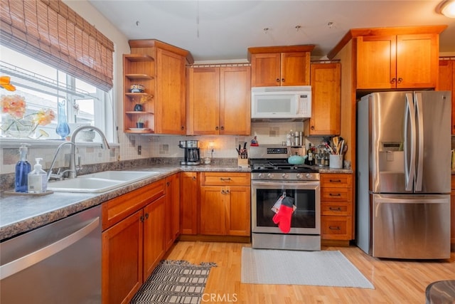 kitchen with backsplash, light wood-style flooring, appliances with stainless steel finishes, and a sink