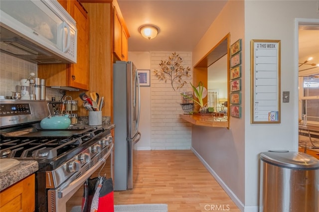 kitchen with baseboards, light wood-type flooring, decorative backsplash, brown cabinetry, and stainless steel appliances