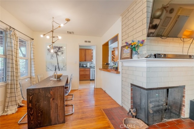 kitchen with dishwasher, a brick fireplace, light wood-style flooring, and visible vents