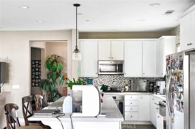 kitchen featuring visible vents, tasteful backsplash, appliances with stainless steel finishes, white cabinets, and hanging light fixtures