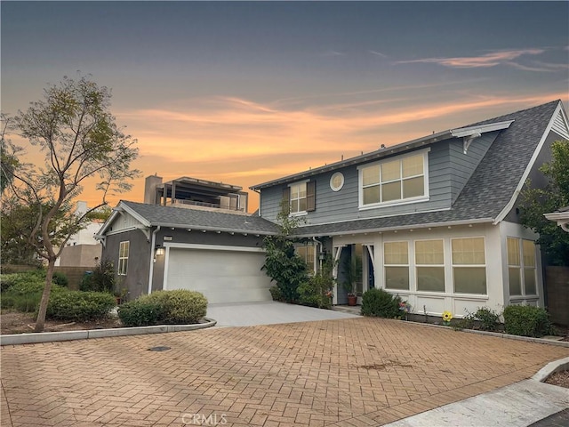 traditional-style house with a garage, decorative driveway, stucco siding, and a shingled roof