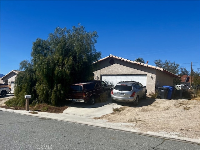 view of side of property featuring stucco siding, an attached garage, driveway, and a tile roof