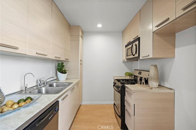 kitchen featuring baseboards, light countertops, light wood-style floors, stainless steel appliances, and a sink