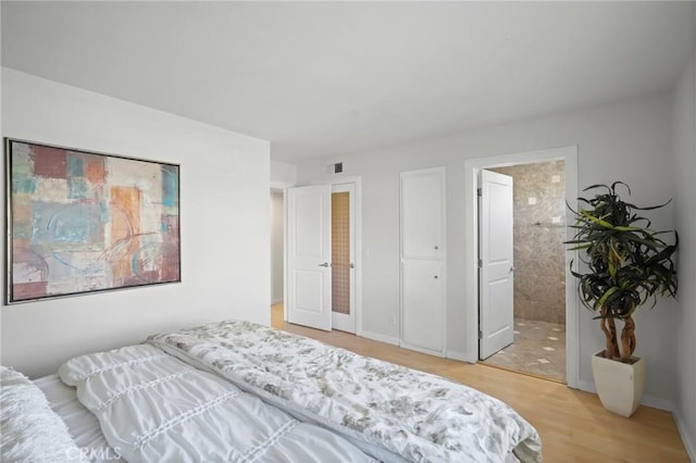 bedroom with light wood-style floors, visible vents, ensuite bathroom, and baseboards