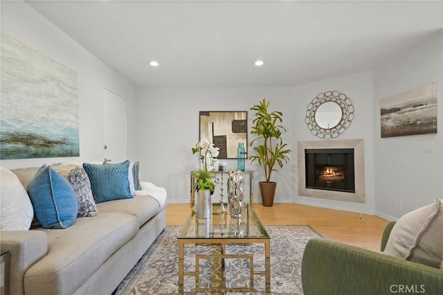 living room with recessed lighting, wood finished floors, baseboards, and a lit fireplace