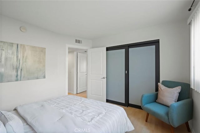 bedroom with light wood-style floors, visible vents, and a closet