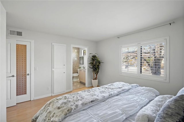 bedroom with connected bathroom, visible vents, and light wood-style flooring