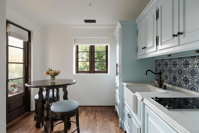 kitchen featuring light countertops, decorative backsplash, wood finished floors, black electric cooktop, and a sink