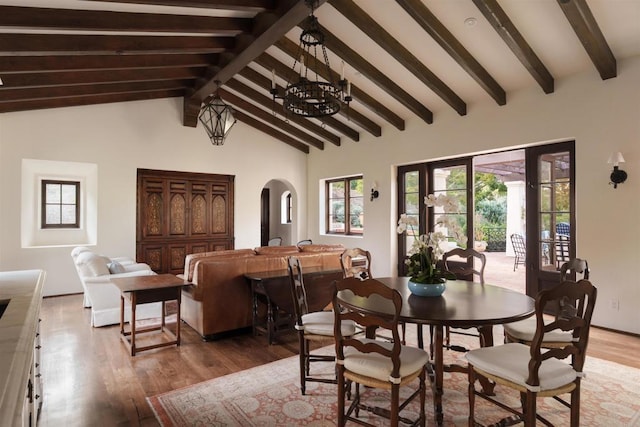 dining area with light wood-style flooring, beamed ceiling, arched walkways, and high vaulted ceiling