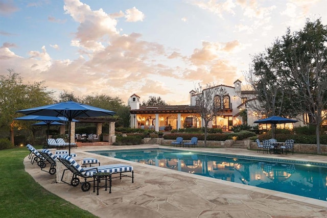 pool at dusk with an outdoor pool and a patio