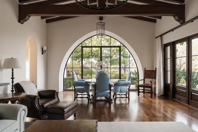 living area featuring arched walkways, plenty of natural light, beamed ceiling, and wood finished floors