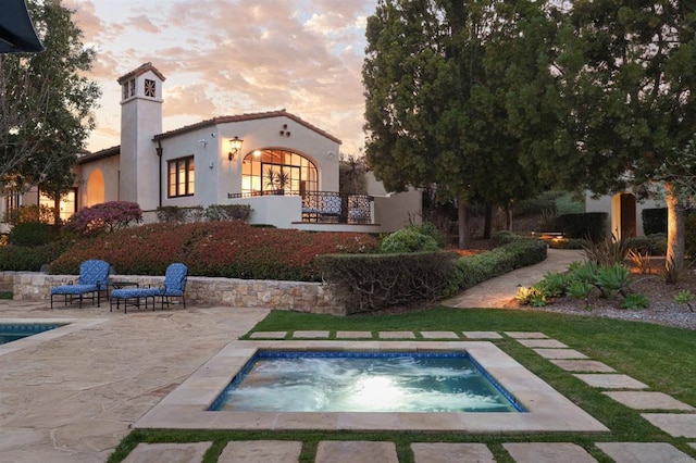 back of house at dusk featuring an in ground hot tub, a tiled roof, a patio area, and stucco siding