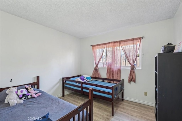 bedroom featuring a textured ceiling, light wood-type flooring, and baseboards