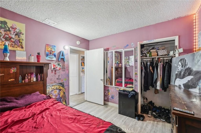 bedroom with wood finished floors, visible vents, a closet, and a textured ceiling