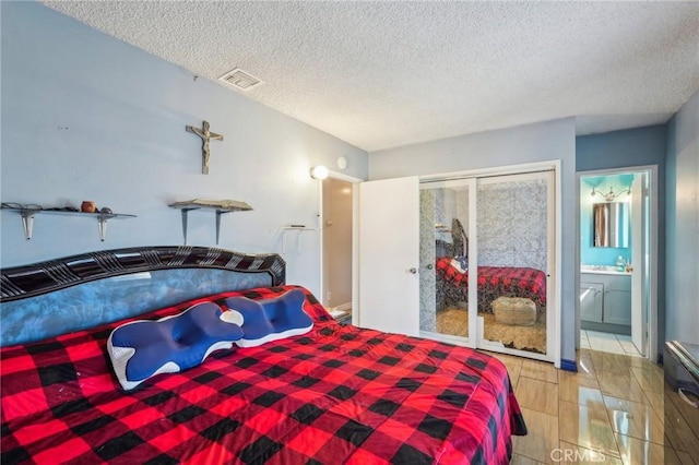 bedroom featuring visible vents, wood tiled floor, ensuite bath, a closet, and a textured ceiling