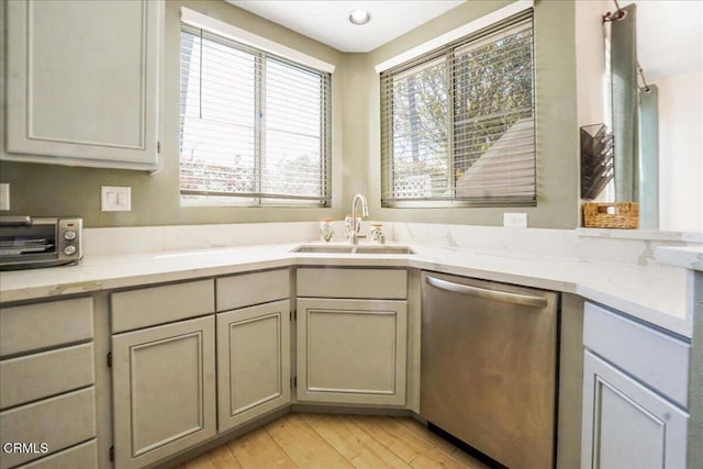 kitchen featuring light wood-style flooring, a sink, stainless steel dishwasher, a toaster, and light stone countertops