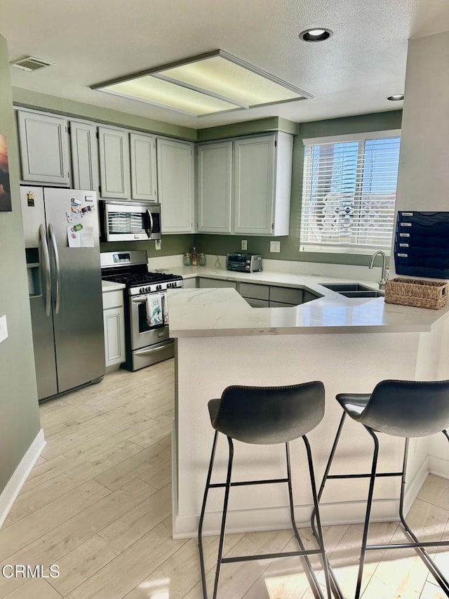 kitchen with a peninsula, a sink, stainless steel appliances, light wood-style floors, and a textured ceiling