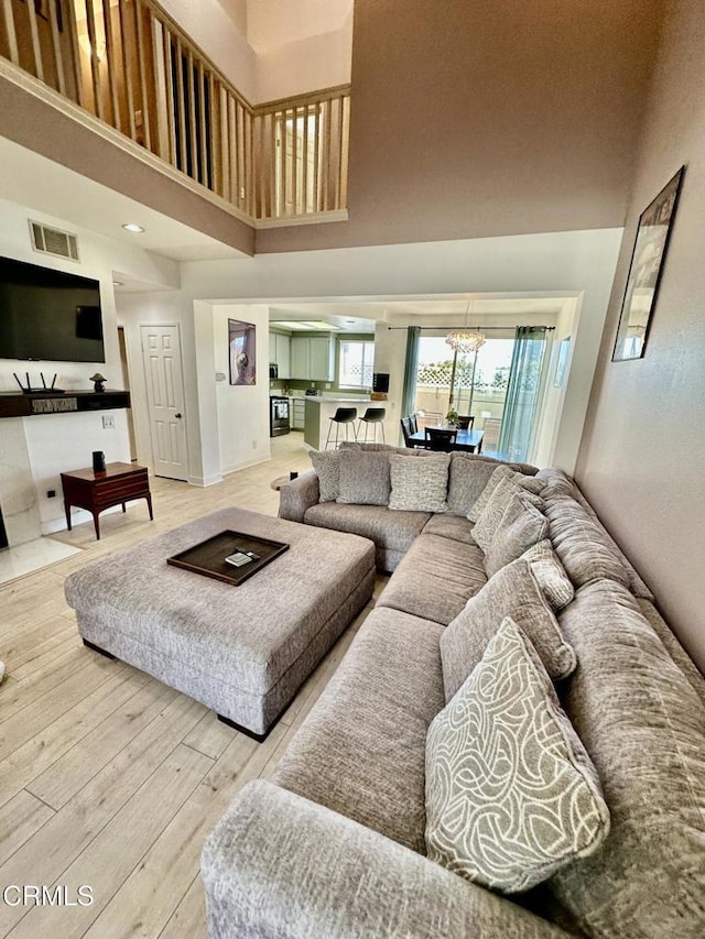 living room with visible vents, an inviting chandelier, wood finished floors, and a towering ceiling