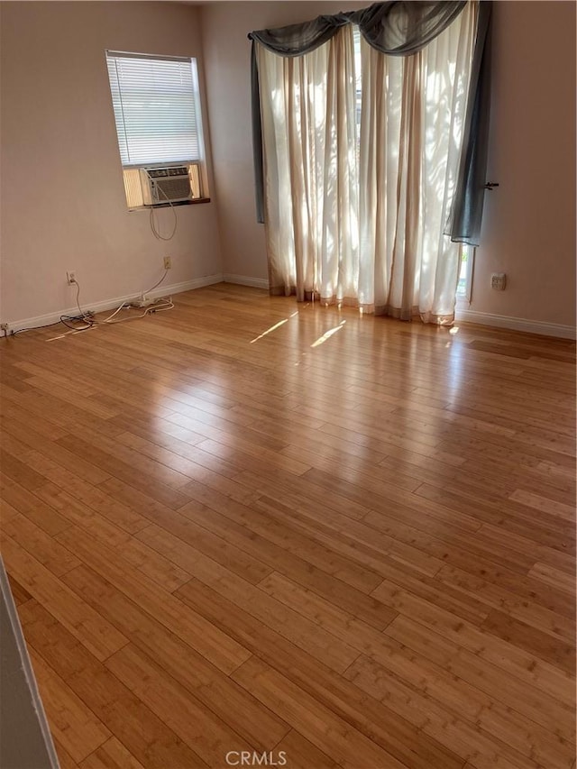 empty room featuring cooling unit, baseboards, and wood finished floors