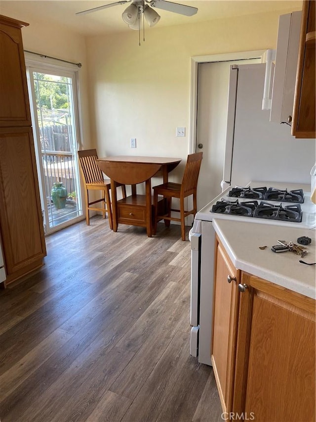 kitchen with a ceiling fan, dark wood finished floors, white appliances, brown cabinetry, and light countertops