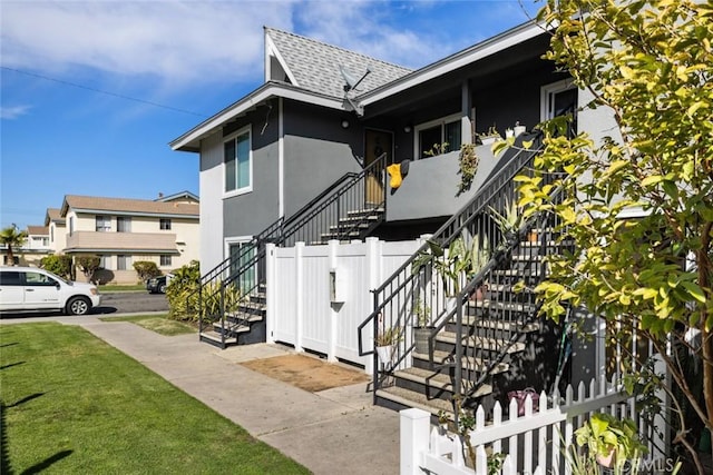 exterior space with stucco siding, a lawn, roof with shingles, and fence