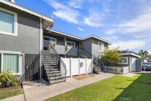 view of front of property with stucco siding, a front yard, stairs, and fence