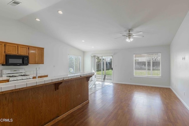 kitchen with brown cabinets, white gas range, black microwave, tile counters, and vaulted ceiling