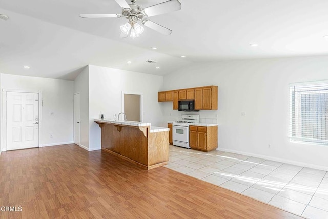 kitchen featuring brown cabinets, gas range gas stove, a peninsula, black microwave, and light countertops